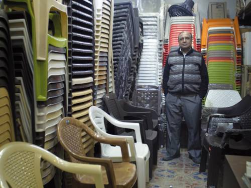 Ein Mann steht in einem Stuhllager in dem Plastikstühle unterschiedlichster Ausführungen gestapelt sind.